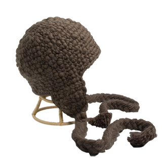 A thick, brown Chunky Knit Long Tassel Earflap hat with long braided tassels resembling a wig, displayed on a stand against a white background.