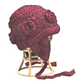 A burgundy wool Crochet Flower Heart Earflap Hat with a tassel is placed on a small wooden stool against a white background.
