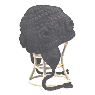 A Crochet Flower Heart Earflap Hat handmade in Nepal with a black knitted wool hat with a pom-pom and braided tassels displayed on a small wooden stool.