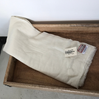 A folded cream-colored Solid Pashmina Scarf with a label is lying in a wooden rectangular tray.