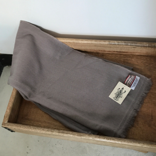A folded Solid Pashmina Scarf with a white tag is placed on a wooden shelf.