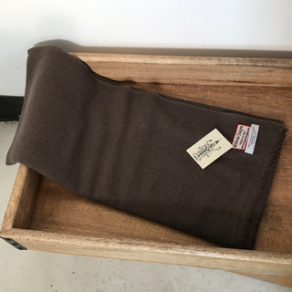 A folded brown Solid Pashmina Scarf with a tag lies inside a wooden drawer.