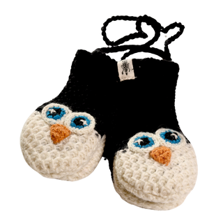 A pair of black and white crochet baby booties with an owl face design on the front, reminiscent of adorable animal puppet mittens. The owl faces are white with blue eyes and orange beaks. Hand-made in Nepal, the booties have a string attached at the top for securing them to each other.