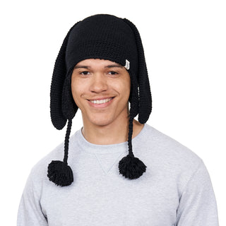 A person smiling at the camera while wearing a Long Ear puppy hat with earflaps and tassels.