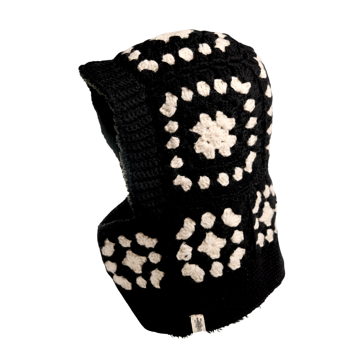 The Hand Crochet Patch Hood is a black and white wool hood, hand-crocheted with a geometric, floral-inspired pattern. It features a tag at the bottom edge and is showcased against a plain white background.