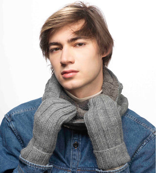 A young man with tousled brown hair wearing a denim jacket and a gray handmade in Nepal ribbed mittens.