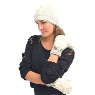 A woman wearing a white knit hat with fleece lining and matching XOXO Fingerless Gloves with Flap, coupled with a black sweater featuring shoulder cutouts, poses with one arm across her body while looking to the side.