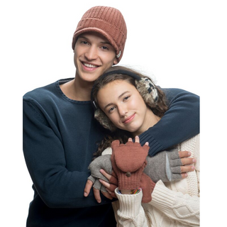 A young man and woman embrace warmly, smiling at the camera while holding a stuffed toy between them. They are dressed in winter clothing, including Merino wool sweaters and Fillmore Cap Visors.