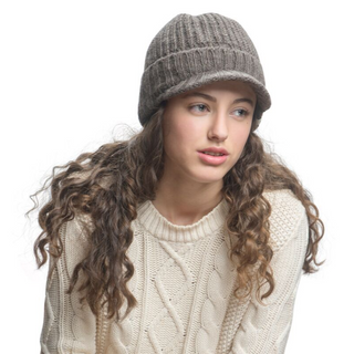 A young woman with curly hair wearing a knit Merino wool Fillmore Cap Visor and cream sweater, looking to the side with a thoughtful expression.