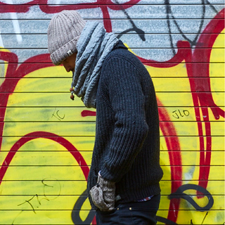 A man wearing a hat and a Lou Neckwarmer in front of a graffiti wall.