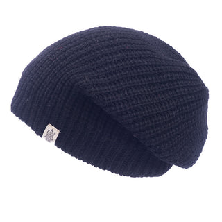The black "Cardigan Knit Slouch" beanie has a waffle texture and is handmade in Nepal from 100% wool. It includes a small white square tag with an emblem on the folded edge, offering a slightly slouched shape for the perfect look.