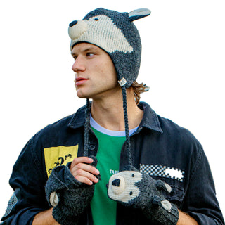 A man wearing a hand-knit Wolf Hat and gloves that resemble a raccoon, looking to the side against a plain background.
