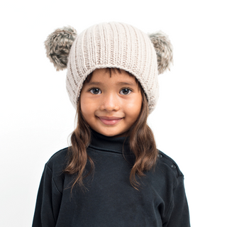A child with a content smile wearing a Double Pom Beanie against a white background.