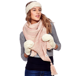 A woman wearing winter accessories, including a handmade cream headband, a pink scarf, and cream mittens made of Trifecta Shawl from Nepal, stands against a white background.