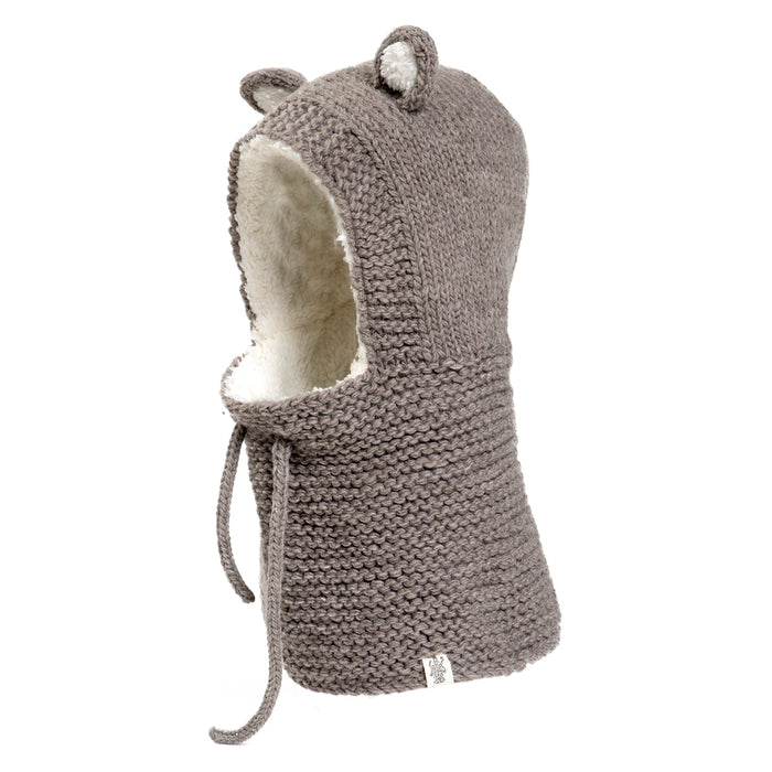 The Hand Knit Teddy Hood is handmade in Nepal from soft gray merino wool and lined with white sherpa fleece. Featuring charming bear ears and a drawstring at the neck, the hood is shown upright against a white background.