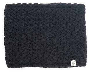 A black textured merino wool I See Stars neckwarmer or fabric with a repetitive pattern and a visible logo label on the bottom right corner.