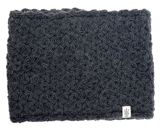 A dark gray crocheted or knitted I See Stars Neckwarmer with a repetitive starburst pattern, featuring a small white tag with a logo on the lower right corner and a sherpa fleece lining.