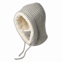 A Hand Knit Glide Hood in gray lambswool with a seed-stitch texture, featuring cream-colored fleece lining and two drawstrings, designed to keep the head and neck warm. Shown against a white background.