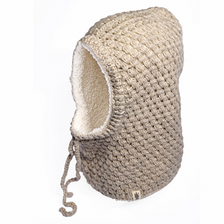 The Hand Crochet Cloud Hood is a beige, textured knit hood made from cozy lambswool with a cream-colored fleece lining. It features a drawstring and a small fabric tag at the bottom edge, and is photographed against a white background.