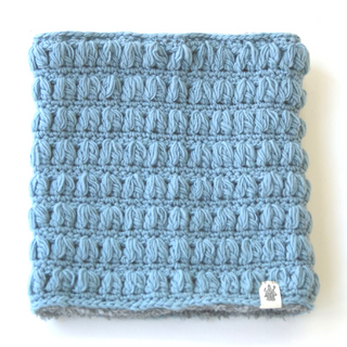 A Good Vibes Neckwarmer handmade in Nepal light blue knitted square with a textured pattern, placed against a white background.