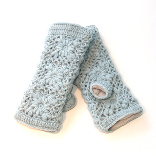 Flower Crochet Handwarmers: Light blue, wool fingerless gloves with a floral crochet pattern and thumb hole. Soft, textured, and ideal for keeping your hands warm on chilly days. Shown laid on a white background.
