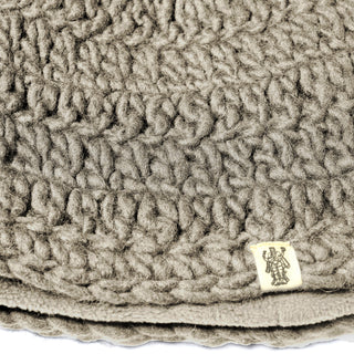 Close-up of the Hand Crochet Acorn Hat, showcasing its textured, chunky-knit design in gray with a small beige fabric tag featuring a black emblem sewn onto one side—its cozy appearance reminiscent of a soft wool winter beanie or chunky blanket, perfect for adding warmth and comfort to any outfit.