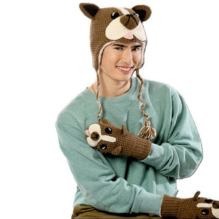 A smiling person is wearing a green sweatshirt and sitting while dressed in a matching Crochet Bulldog Hat and mittens. The handmade in Nepal hat and mittens feature a brown and beige design with an animal face, ears, and paws, possibly resembling a bulldog.