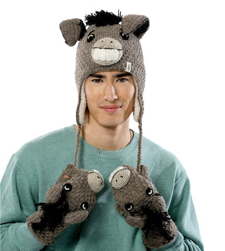 A man wearing a green sweater and a knitted donkey hat is holding up Crochet Donkey Mittens. The handmade in Nepal hat and mittens feature donkey faces with ears, eyes, and mane details. The background is white.