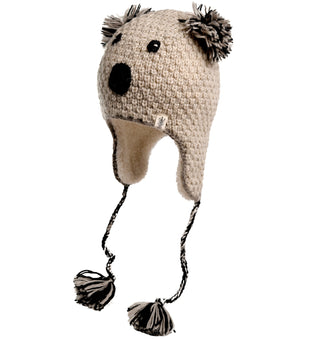 The Crochet Koala Hat, hand-made in Nepal, is designed to resemble a bear's face and features black eyes, a black nose, and ear flaps with braided ties ending in pom-poms. The hat is beige with gray and black details.