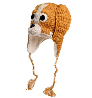 The Crochet Lucy Puppy Hat is a handmade creation from Nepal, designed to resemble a dog's face. It features floppy ears, two large eyes, and a nose crafted from crochet wool. The hat is brown with white details and includes ear flaps with braided tassels hanging down for added charm.