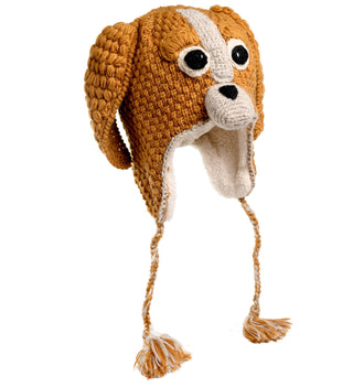 The Crochet Lucy Puppy Hat is a crocheted wool hat designed to resemble a dog's head, featuring floppy brown ears, large black and white eyes, a white snout with a black nose, and braided tassels hanging from each side. Handmade in Nepal, the inside is lined with soft sherpa fabric for ultimate comfort.