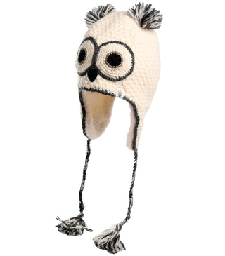 The Crochet Owl Hat is a cream-colored, hand-made accessory designed to resemble an owl. It features two black eyes, a small black beak, and two ear flaps with braided strings ending in tassels. The top has two small pom-poms resembling owl ears, adding a charming touch to this woolen hat.