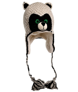 The Crochet Rockey Racoon Hat is a handmade knit hat with ear flaps, crafted in Nepal. The hat portrays a racoon's face and is predominantly white with black and green detailing for the eyes, nose, and mouth. It features black and white braided strings with tassels at the ends and a warm sherpa lining for added comfort.