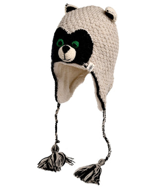 The Crochet Rockey Racoon Hat is a handmade beige knit hat, crafted in Nepal from crochet wool. It showcases a black and white raccoon face with green eyes, black ears on top, and braided tassels hanging from the ear flaps.