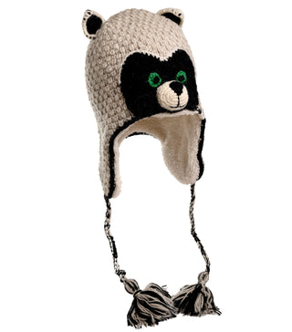 The Crochet Rockey Raccoon Hat, handmade in Nepal from crochet wool, is a beige knit hat with ear flaps and braided tassels. It features a black and white panda bear face design with green eyes on the front and has two small ears on top.