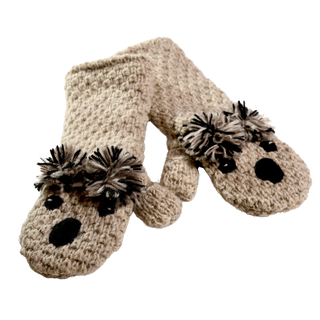 The Crochet Koala Mittens, crafted by hand in Nepal, are a charming pair of beige mittens featuring adorable animal faces with black eyes and noses, complemented by pom-poms resembling ears on the back. These mittens, made from 100% wool, are showcased against a simple black background.