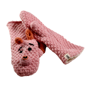 A pair of Crochet Piggy Mittens made from pink, crochet wool. One mitten showcases a charming design resembling a face with two small orange horns, eyes, eyebrows, and a nose. Handmade in Nepal using textured yarn, these mittens also include a small tag with an indiscernible logo.