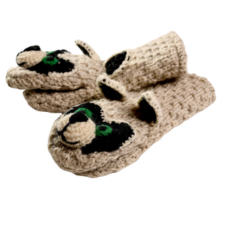 The image shows a pair of beige Crochet Rockey Racoon Mittens, handmade in Nepal, designed to resemble raccoon faces. The mittens feature black and green detailing for the eyes and ears, as well as black patches around the eyes typical of a raccoon.