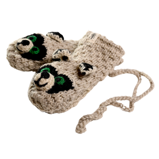 A pair of Crochet Rockey Racoon Mittens, tan-colored and designed with raccoon faces. The raccoons have black and green eyes and black ears. Handmade in Nepal, these crochet wool mittens are joined by a knitted string.