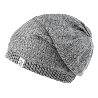 The Hand Loom Dekalb Slouch is a gray slouchy beanie with a ribbed band and small white logo tag, hand-knit for a relaxed, cozy look and shown laid flat at an angle.