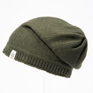 The Dekalb Slouch is a dark green hand-knit beanie with a folded brim and a small white side tag, shown against a plain white background.