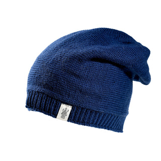 The Dekalb Slouch is a blue, hand-knit beanie hat crafted from soft merino wool, featuring a small white rectangular tag sewn onto its ribbed brim and shown against a white background.
