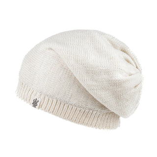 The Dekalb Slouch is a cream-colored, hand-knit beanie for cold weather, featuring a ribbed edge and small metal tag on the cuff, shown against a white background.