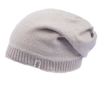 The Dekalb Slouch is a light beige merino wool slouch hat with a ribbed edge and a small graphic fabric tag. Unisex, stylish, and cozy, it's perfect for cold weather and shown here against a white background.
