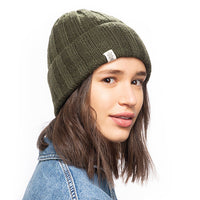 A person with shoulder-length brown hair wearing a Hand Loom Ribbed Beanie in green merino wool and a blue sherpa fleece lined denim jacket looks over their shoulder against a plain white background.