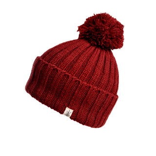 Introducing the Park Fold Rib Pom Beanie: a red, handmade beanie featuring a large pom-pom on top. The beanie showcases a ribbed pattern and a folded brim, beautifully crafted from cozy merino wool. A small white label is sewn onto the brim for an added touch of detail.