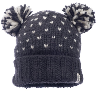 The Double Pom Kira Hat is a knitted dark gray wool hat with white heart-shaped patterns, a folded brim, and two large black-and-white yarn pom-poms on top.