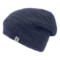 The Hand Knit Boho Slouch is a dark gray, knitted wool beanie with a slightly slouchy silhouette, displayed on a white background. This handmade hat features a small rectangular logo tag on the lower ribbed edge.