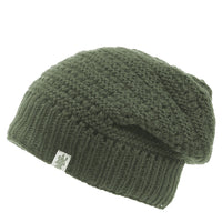 The Hand Knit Boho Slouch is displayed against a white background. This olive green beanie features a slouchy design, a ribbed band, and a small rectangular tag attached to the side of the band.