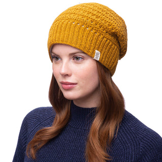 A woman wearing a mustard Boho slouch beanie and wireless earbuds.